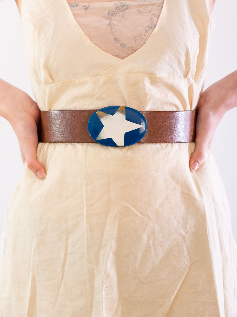 close up of models waist wearing a brown leather belt with a blue oval buckle set with a bone star shape.