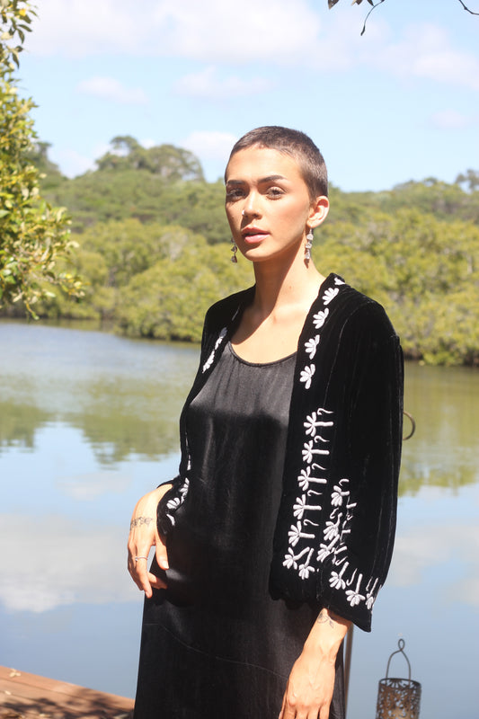 Woman wearing a black silk velvet jacket with white embroidery