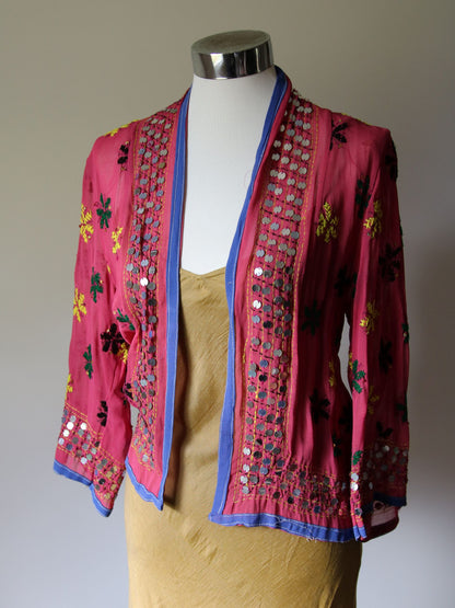 A musk pink  jacket with blue trim and sequins over a silk slip