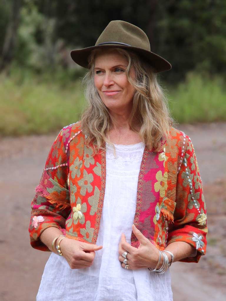 Front view of lady wearing fringed wool jacket in orange with daisies