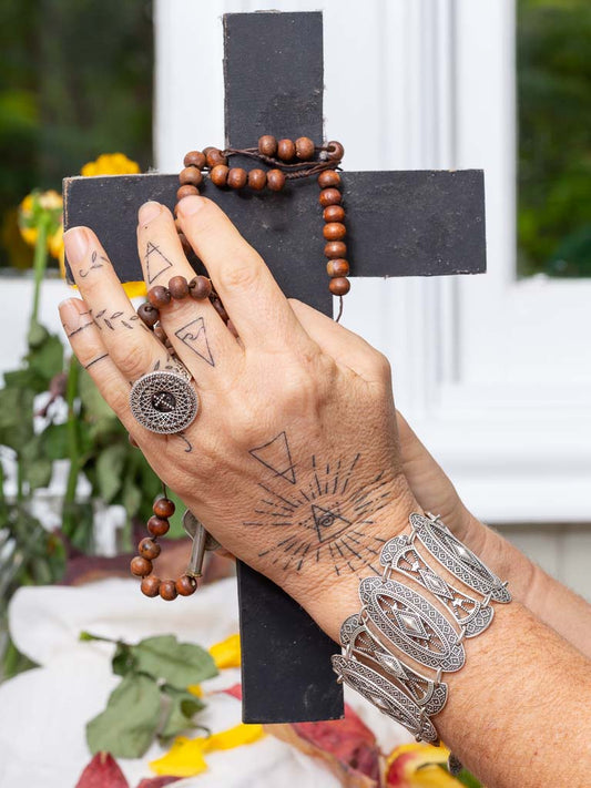 A person with tattooed hand holding a cross with a cross ring 