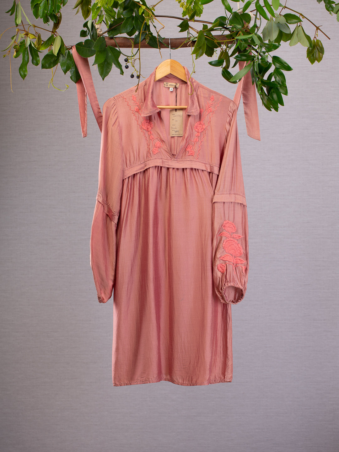 This light and flowing blend of materials compliments the cut of this comfortable dress, flower designs are subtley embroidered on the sleeve and collar in peach thread. Dress hanging from vines