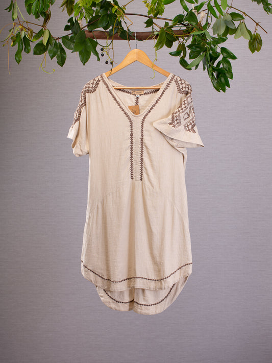 Natural linen dress, embroidered with intricate patterns on the short sleeves and boho arrows bordering the neck and hem in dark grey could be worn casually to the beach or dressed up with accessories and worn to a bohemian wedding. Cream linen dress hanging from vines.