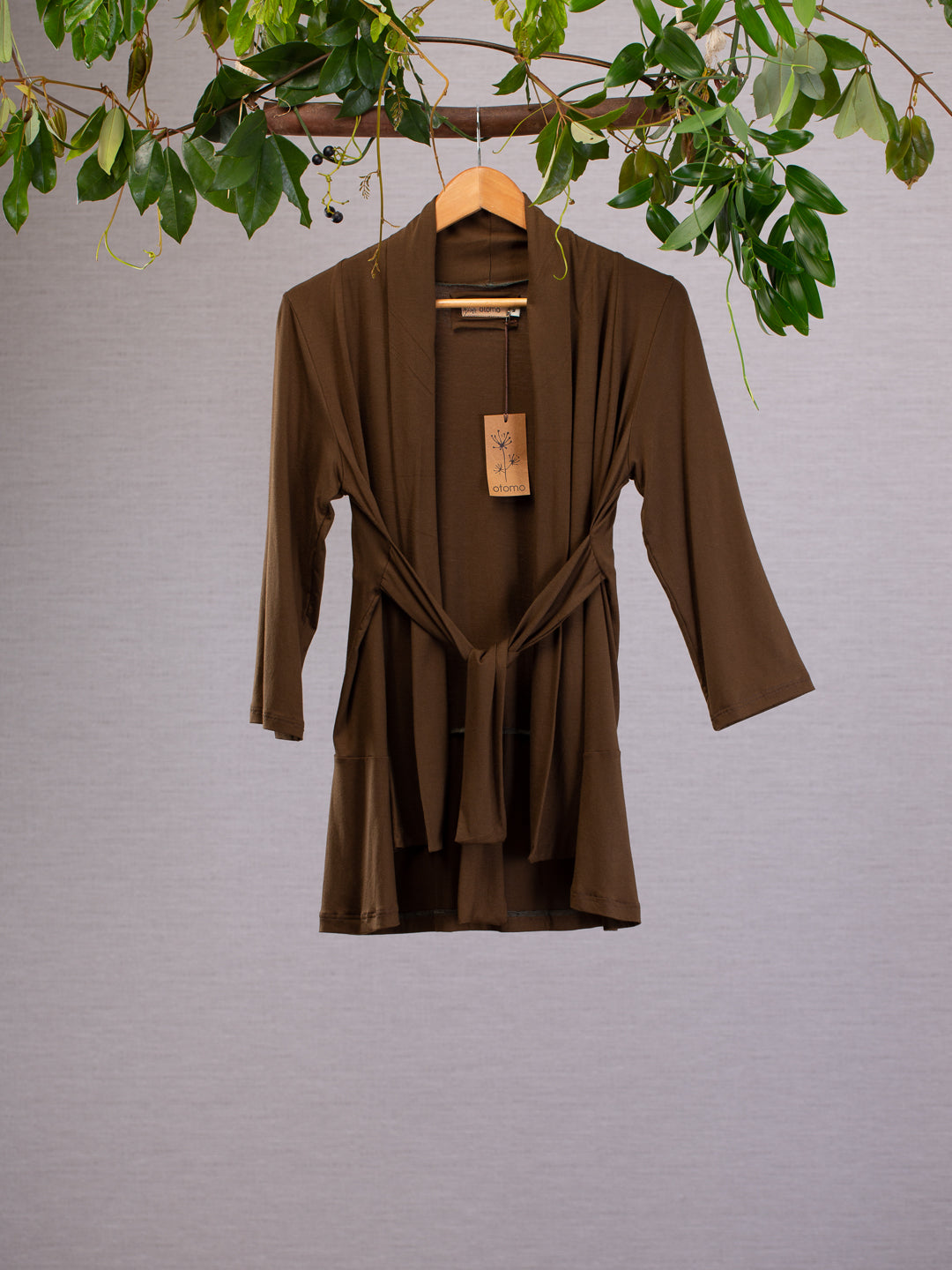 Olive coloured jacket hanging on a hanger, with sashes tied at the front