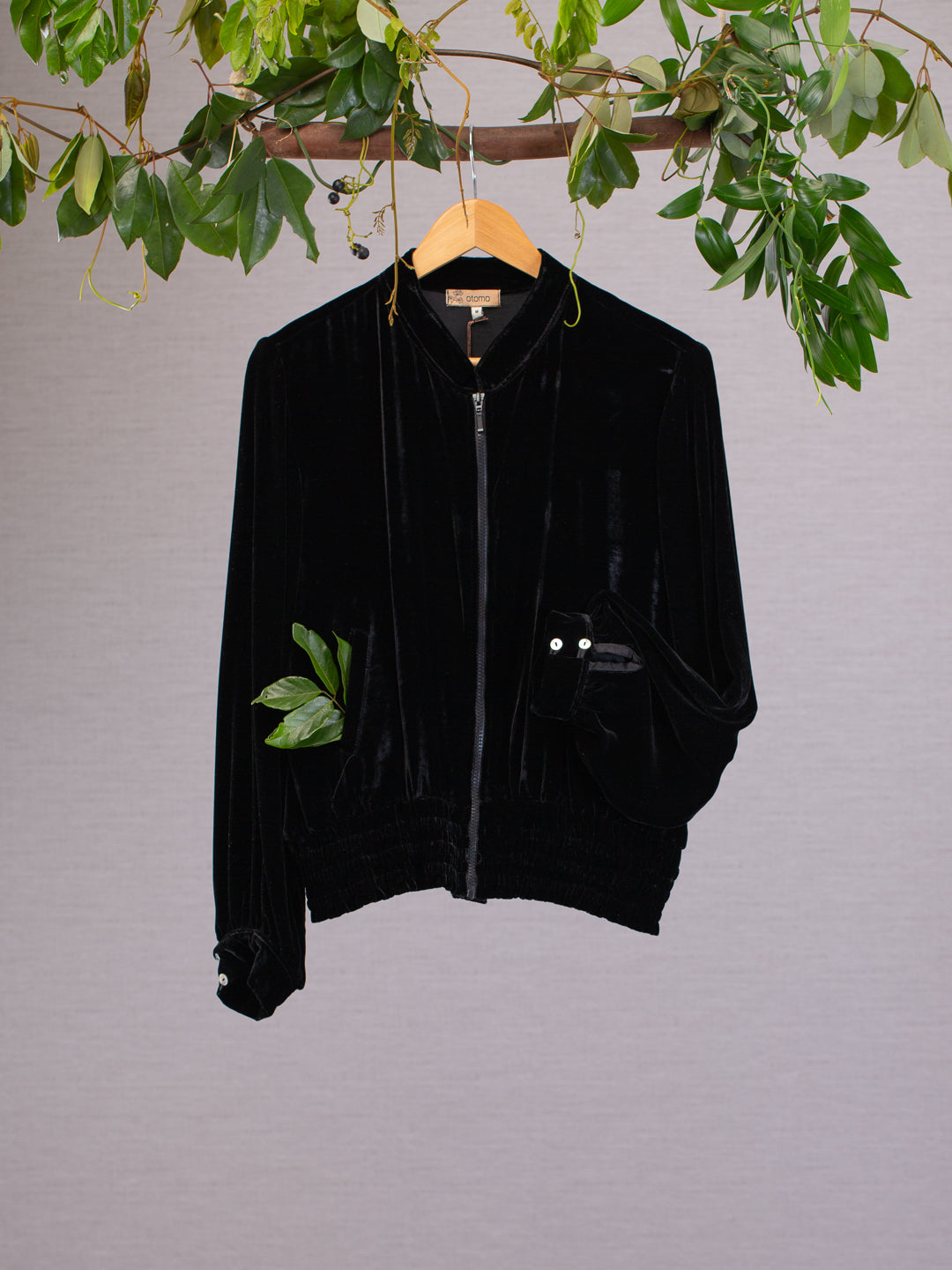 Black silk velvet jacket hanging from vines with a leaf in the pocket, featuring cuff with shell buttons.
