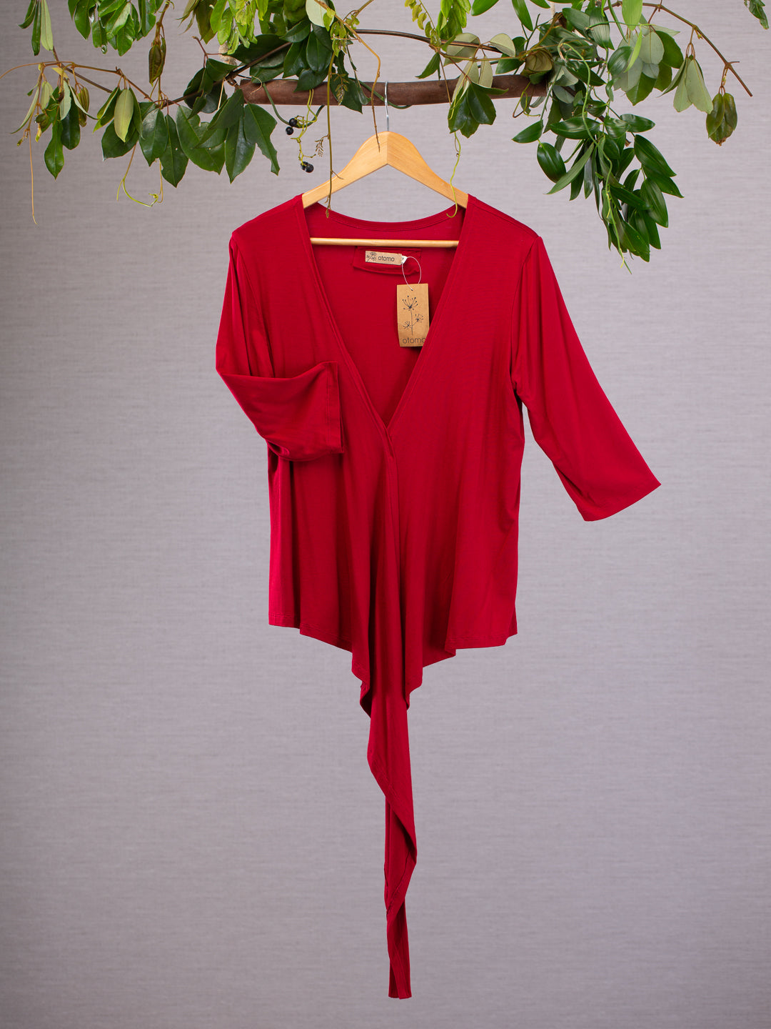 Red wrap-around top hanging on a hager with vines above.