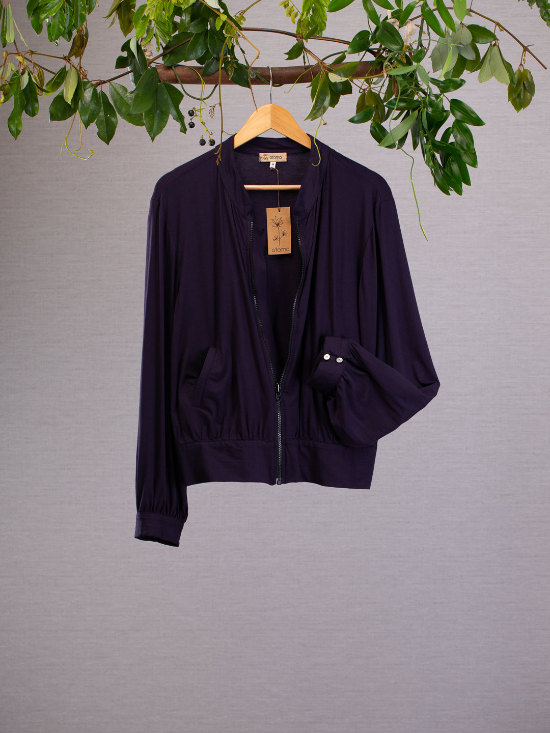 Charcoal bomber jacket hanging on vines displaying the cuff with small shell buttons.